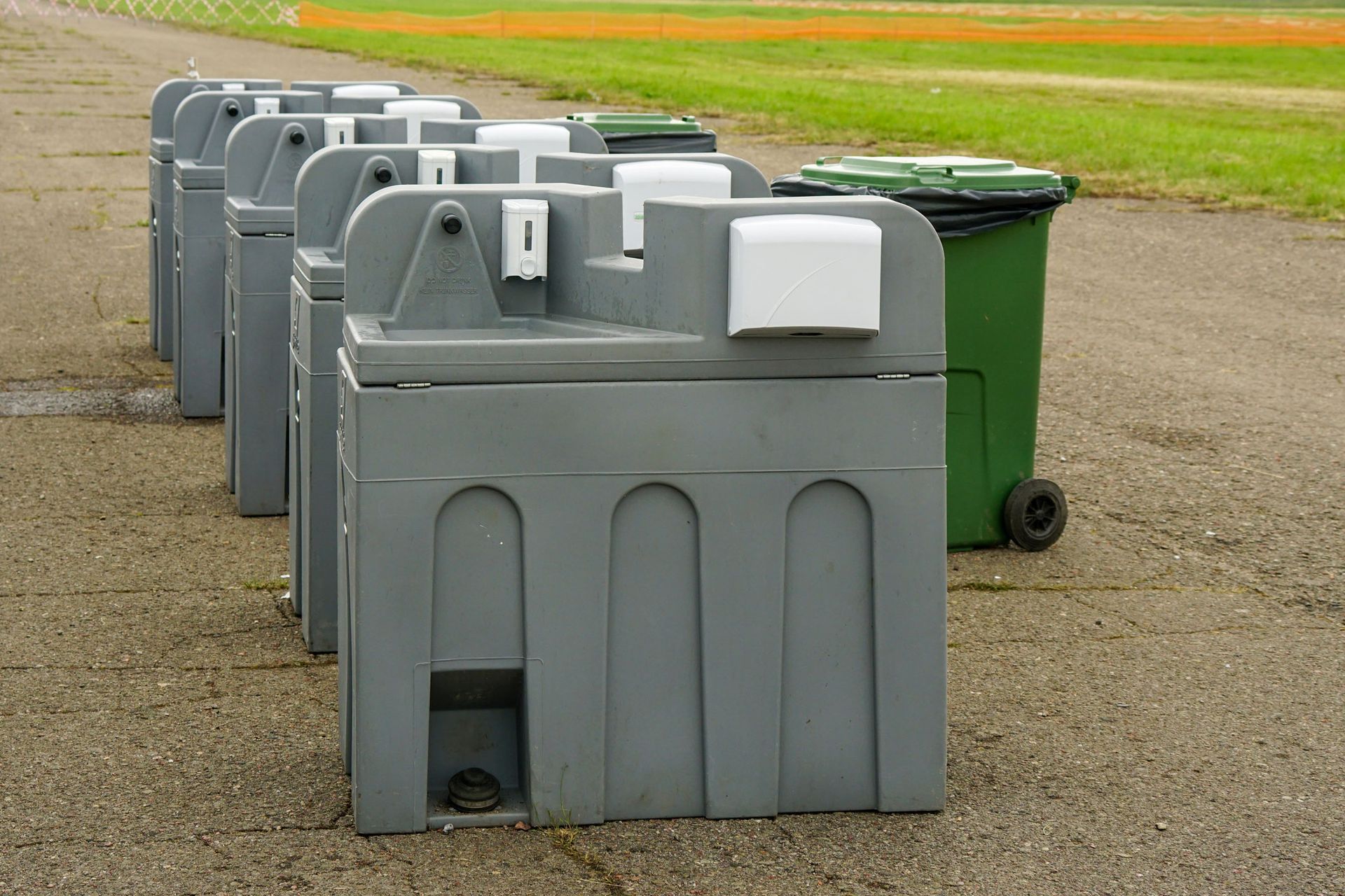 A row of portable sinks and trash cans are lined up on the side of a road.