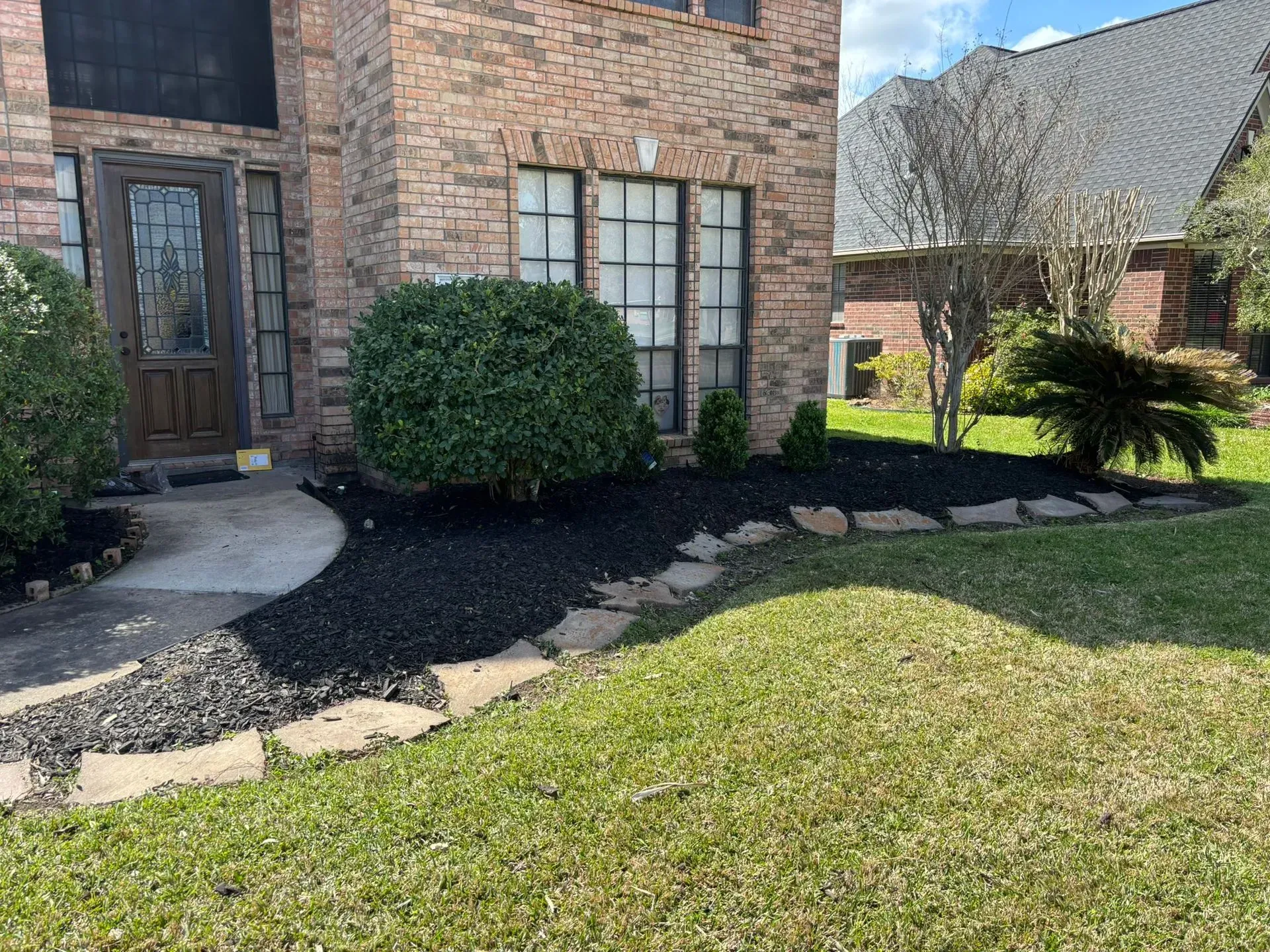 A brick house with a landscaped front yard, featuring dark mulch, stone pathway, and green lawn.