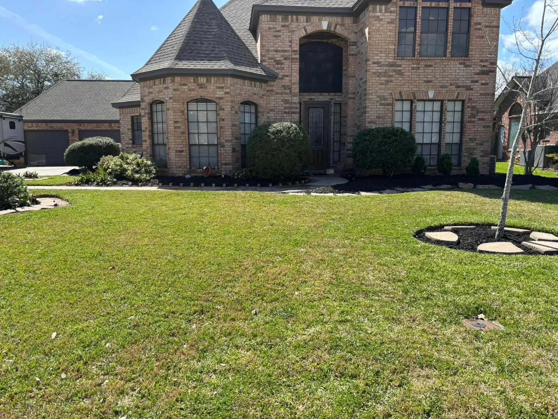 Green grass, bushes, and a tree with a black mulch ring are in the front yard.