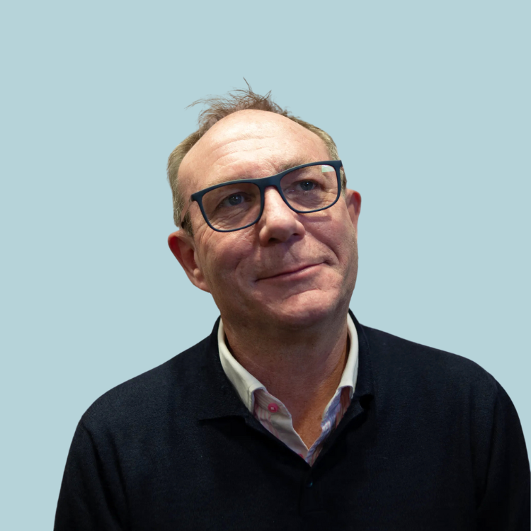 Man with glasses looking up, wearing a dark sweater over a white collared shirt, light blue background.