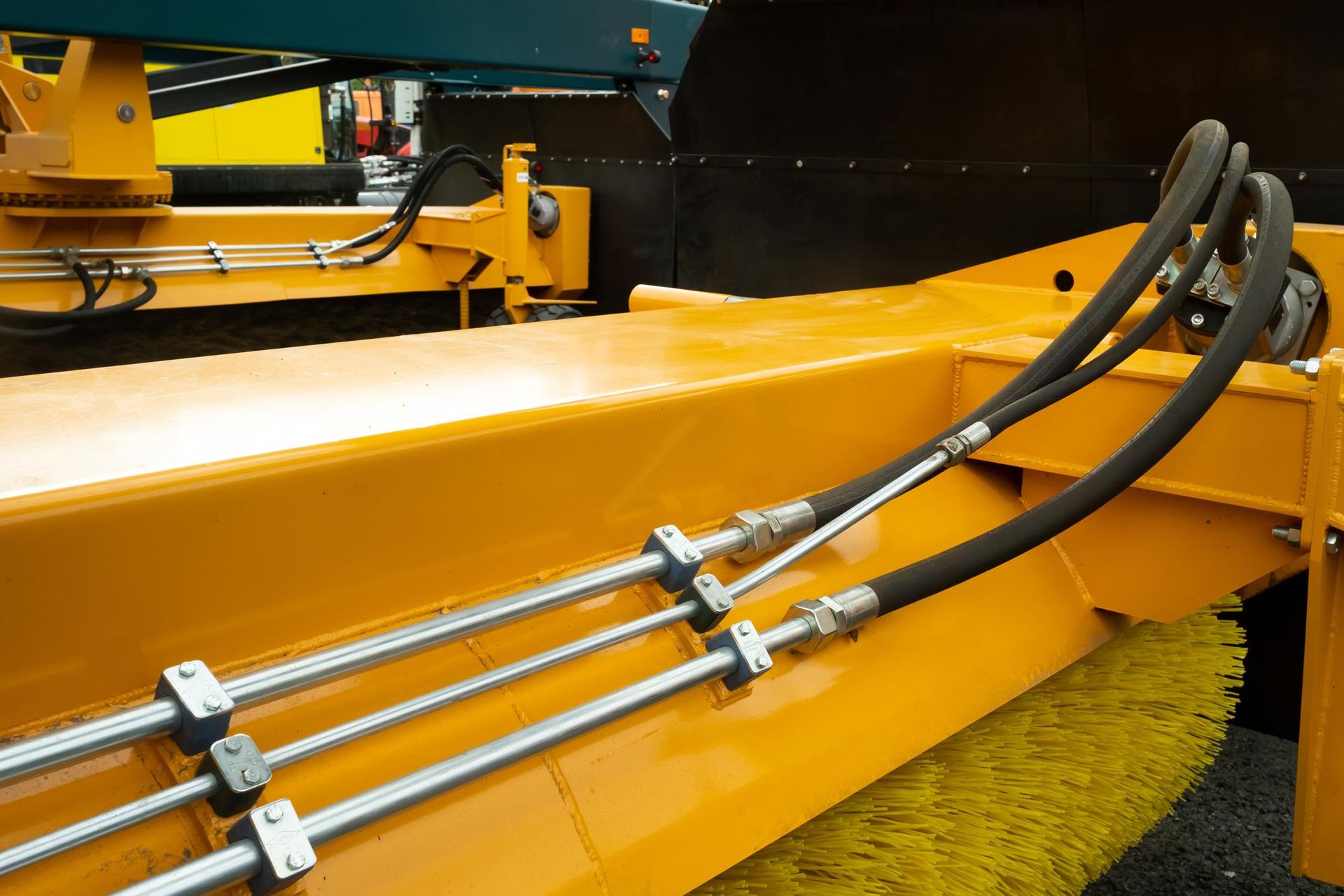 A close up of a yellow broom with hydraulic hoses attached to it