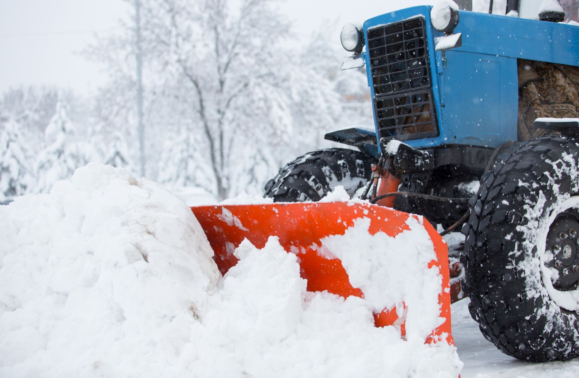 A blue tractor is plowing snow on a snowy road.