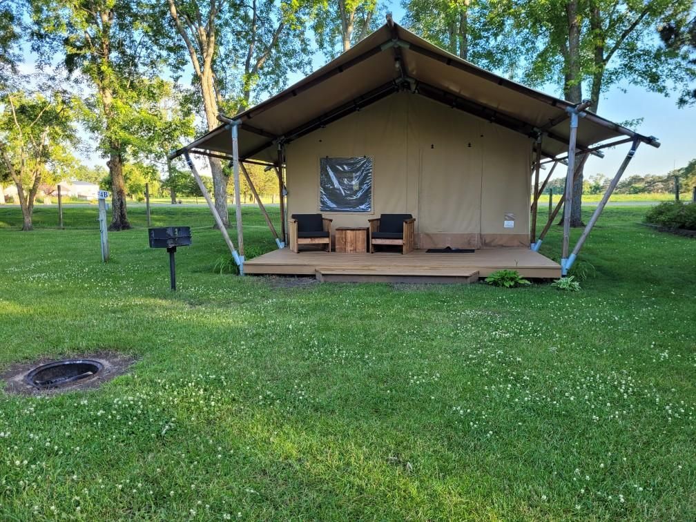 A picture of a large canvas tent with a deck, two chairs and a table.