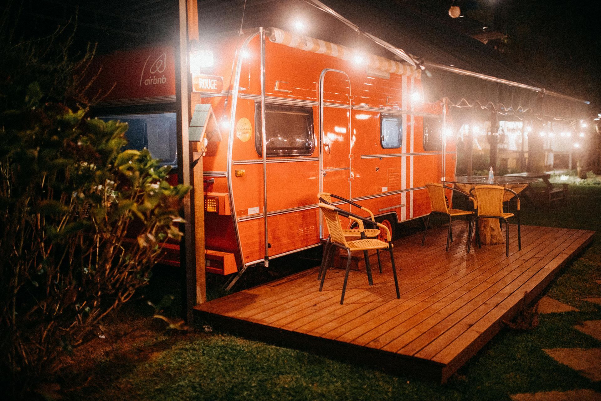 A vintage camper and a deck at night with soft white lights