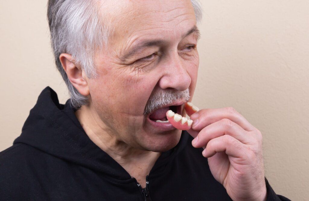 Man Inserting Dentures Into His Mouth — The Denture Care Group Sunshine Coast in Caloundra, QLD