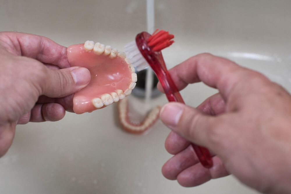 Person Cleaning Dentures With a Brush in a Sink — The Denture Care Group Sunshine Coast in Caloundra, QLD