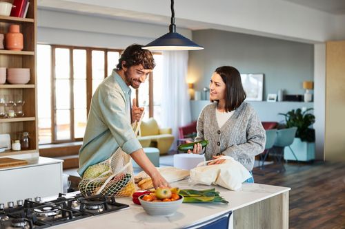 Una gru carica materiali di scarto in un cassone blu su un camion contro un cielo azzurro.