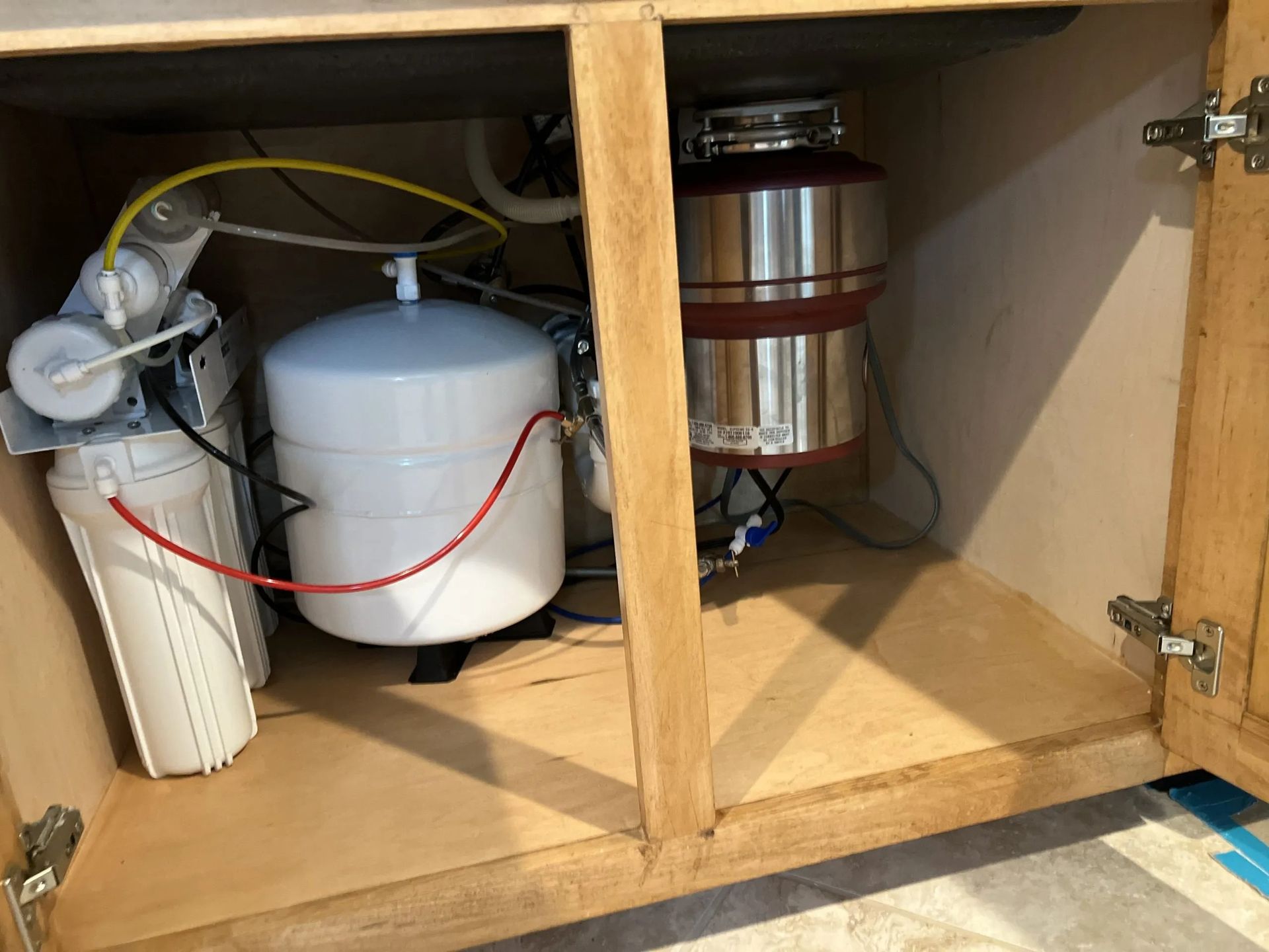 Under-sink cabinet containing a water filter system, a water tank, and a garbage disposal.