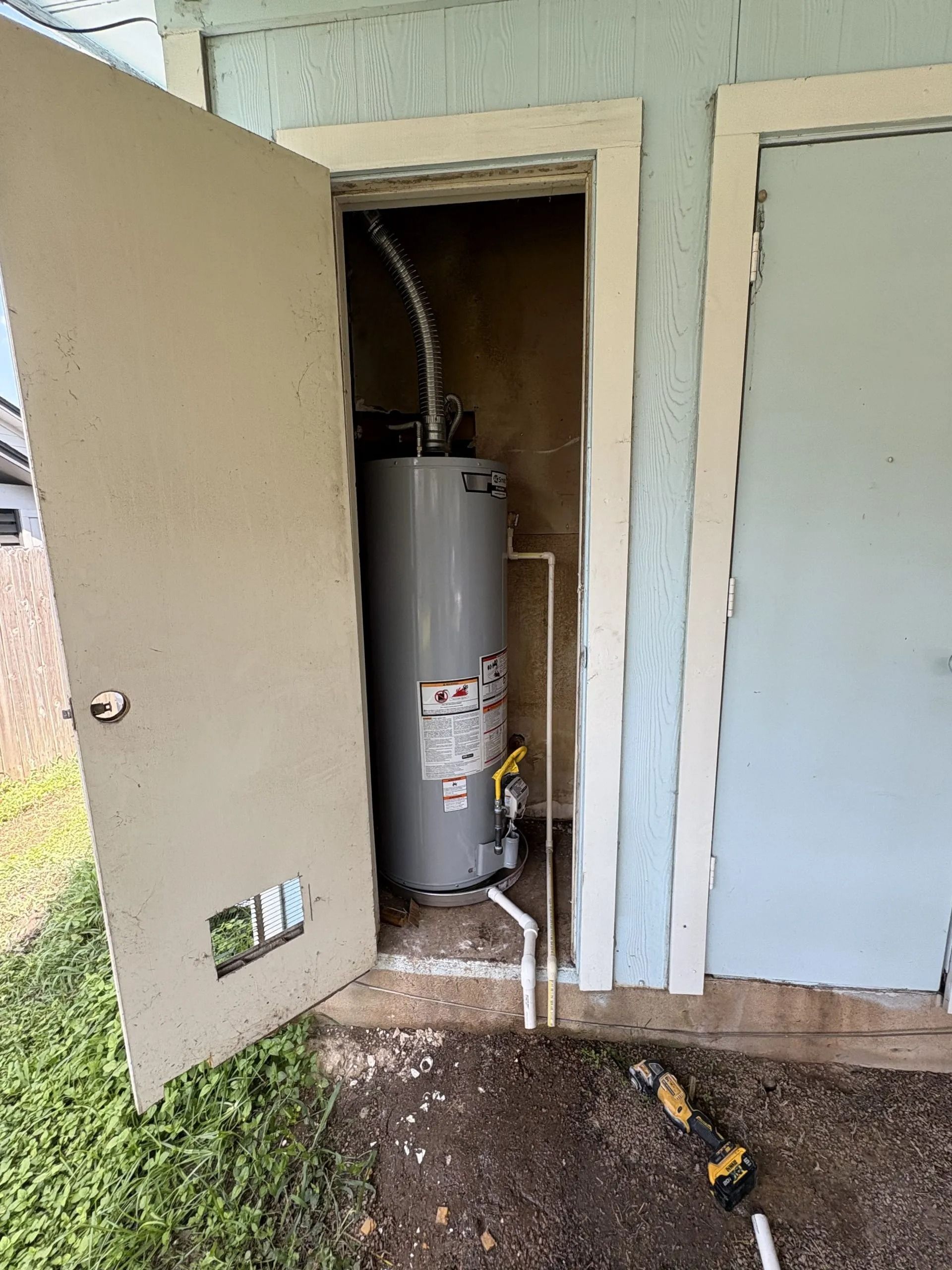Water heater inside a small closet, door open. Pipes and vents visible. Gray tank against a tan wall.