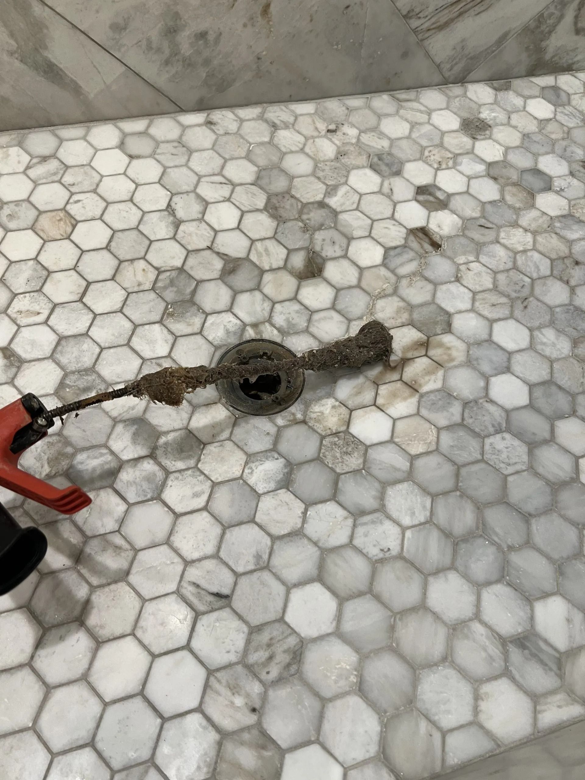 Drain cleaning tool on a white and gray hexagon tile shower floor.