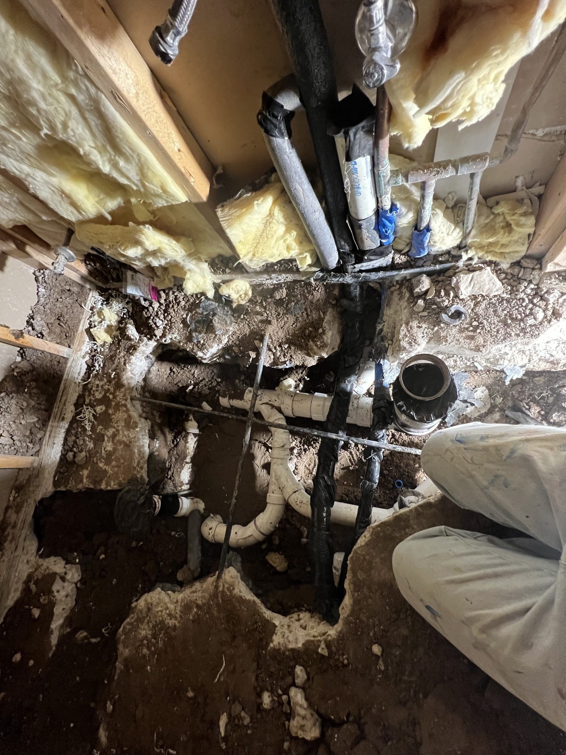Plumbing pipes exposed in a ceiling. Black and white pipes are visible, with insulation and wood.