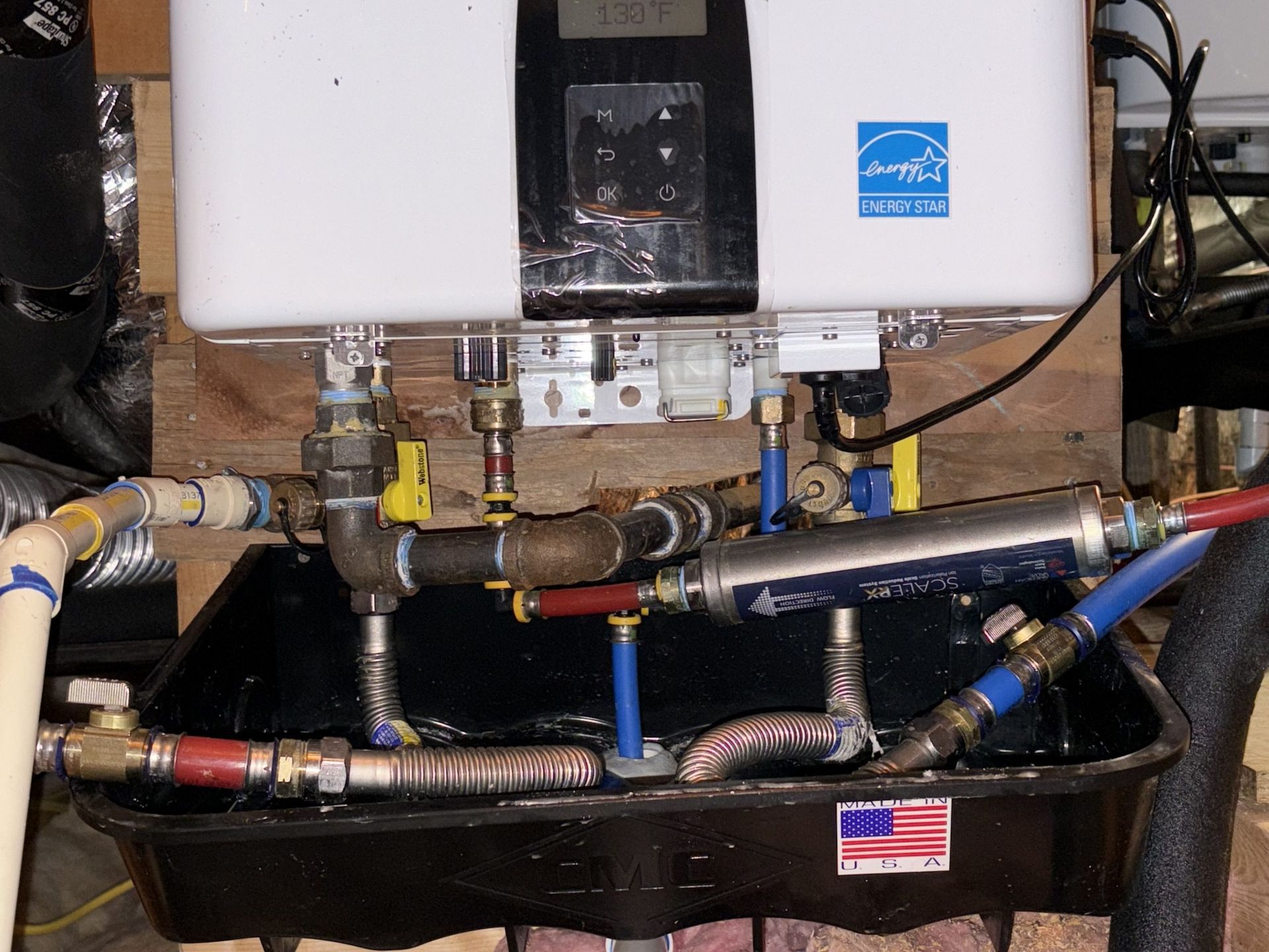 Tankless water heater with connected pipes, installed on wooden supports, in a basement.
