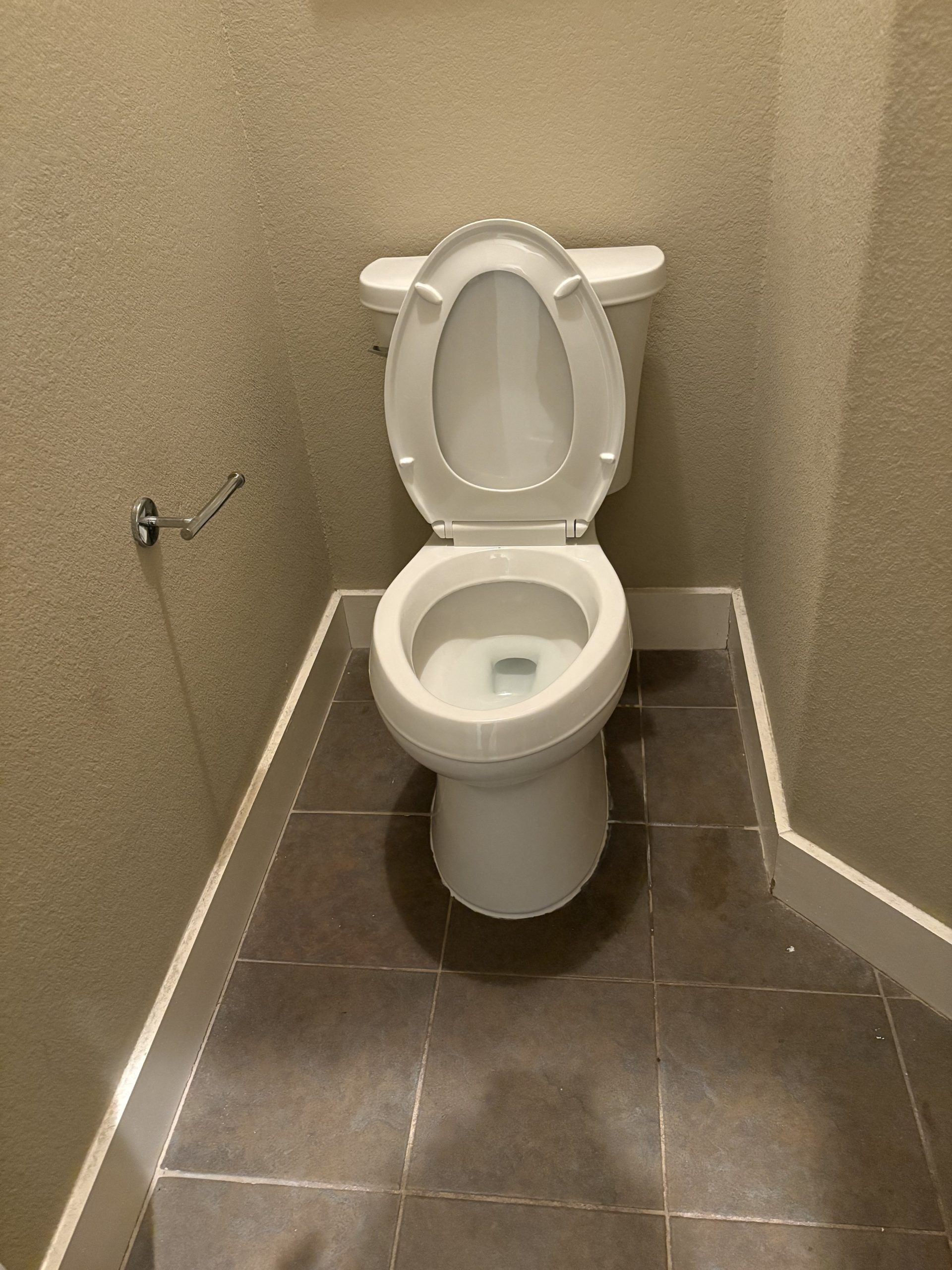 A white toilet with the seat up, in a small bathroom with tile floor and textured walls.