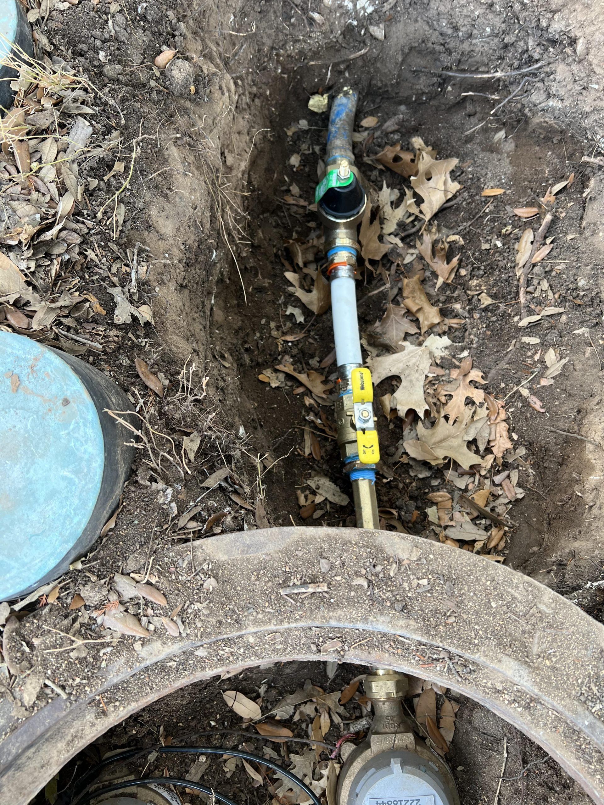 Water pipe assembly in a dirt trench, with a water meter below and connecting parts.