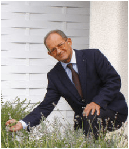 Ein Mann in Anzug und Krawatte pflückt Blumen in einem Garten.