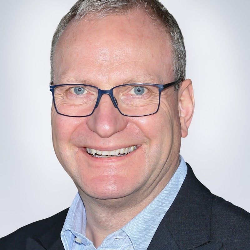 Ein Mann mit Brille und Anzug lächelt in die Kamera.