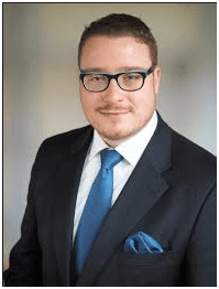 Ein Mann in Anzug und Krawatte trägt eine Brille und ein blaues Einstecktuch.