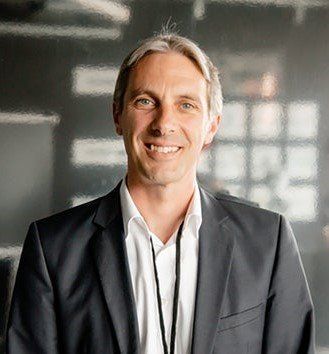 Ein Mann in Anzug und Krawatte lächelt in die Kamera.