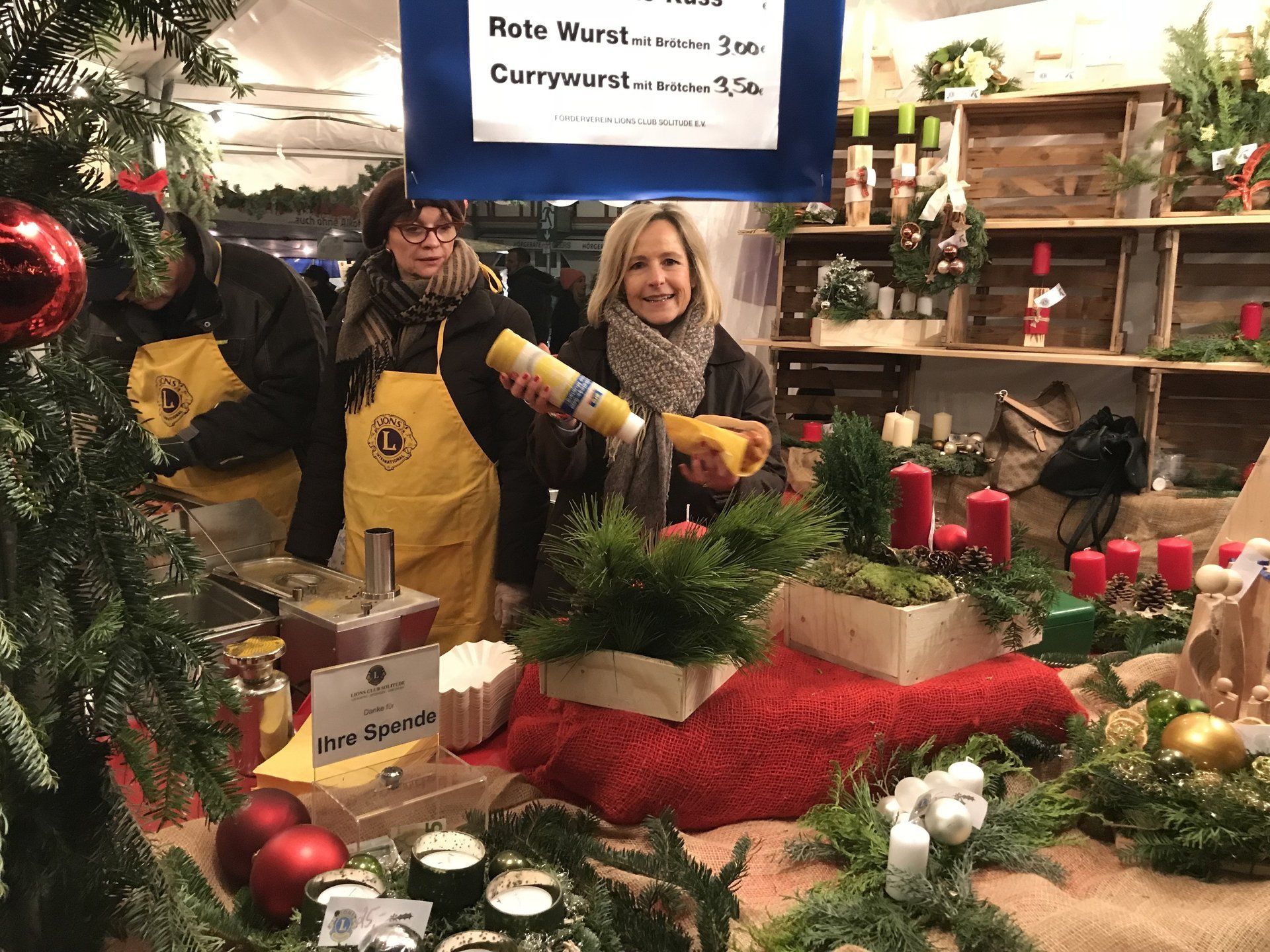 Zwei Frauen in gelben Schürzen stehen vor einem Weihnachtsbaum.