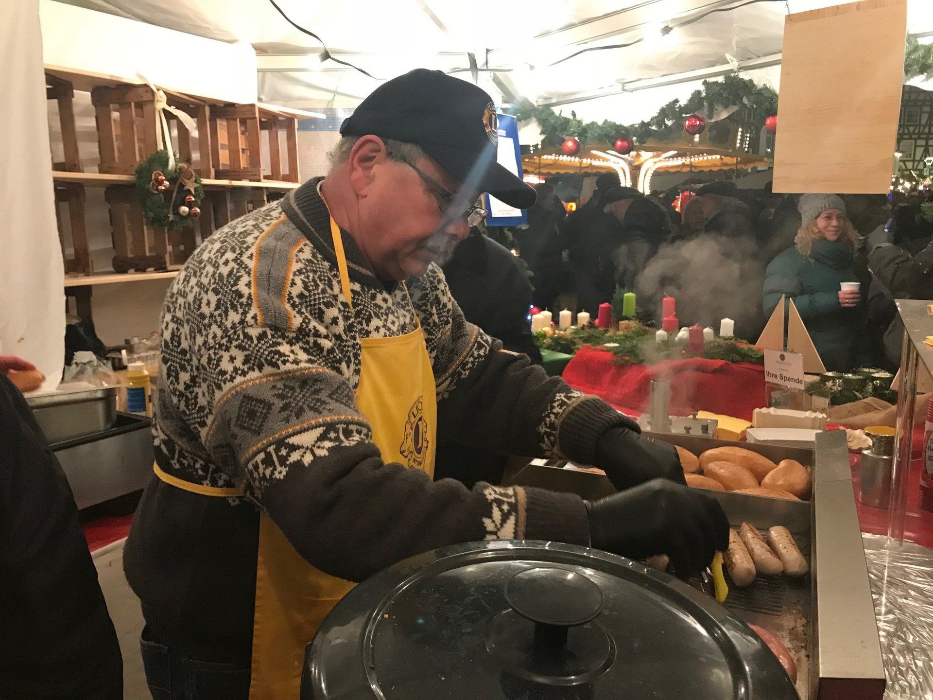 Auf einem Weihnachtsmarkt kocht ein Mann Hot Dogs in einem Topf.