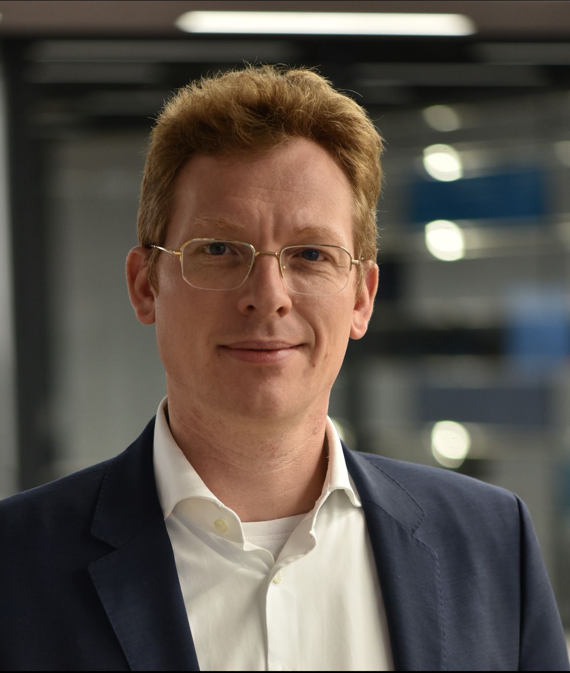 Ein Mann mit Brille und Anzug lächelt in die Kamera