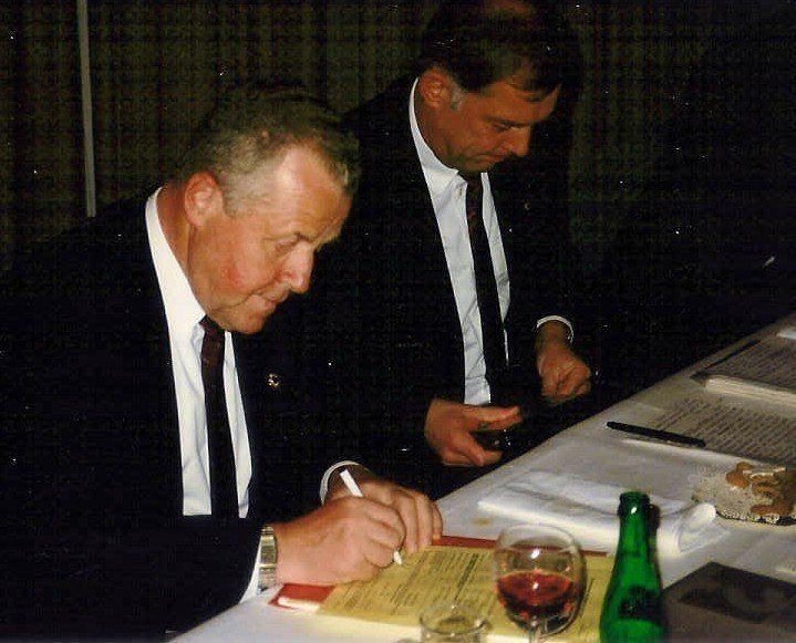 Zwei Männer sitzen an einem Tisch und schreiben auf ein Stück Papier