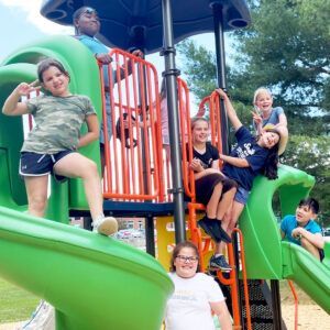 Children playing on a green playground slide, posing and smiling outdoors.