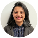 Woman in a blazer smiles, in front of a white wall.