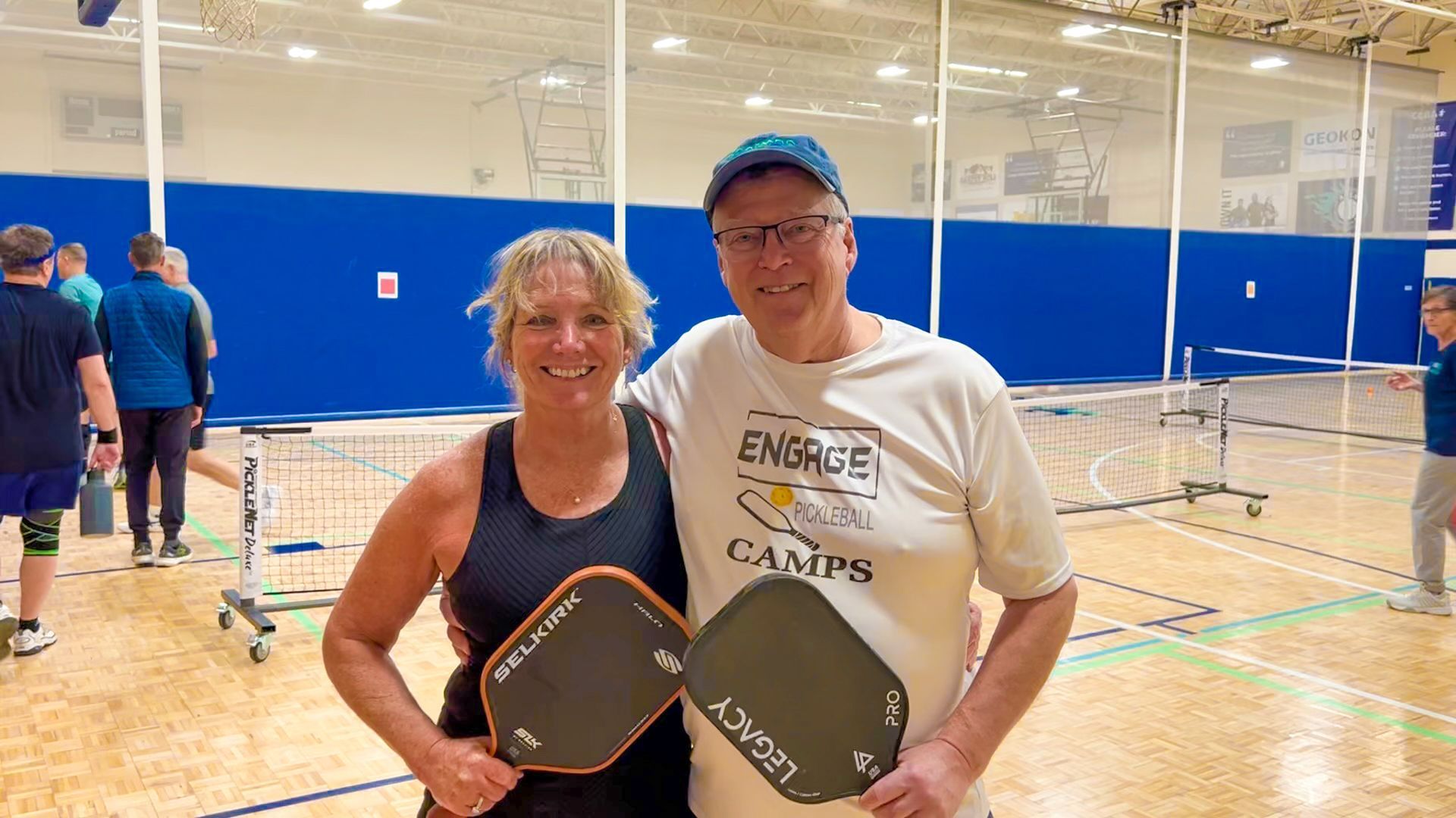 Two people with pickleball paddles pose for a photo in a court, smiling.