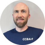 Man with a goatee smiling, wearing a blue shirt with a zipper and the word 