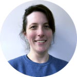 Woman smiling, wearing a blue sweater, against a pale blue background.