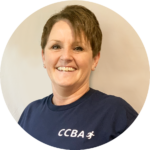 Woman with short brown hair smiles, wearing a navy blue shirt with 