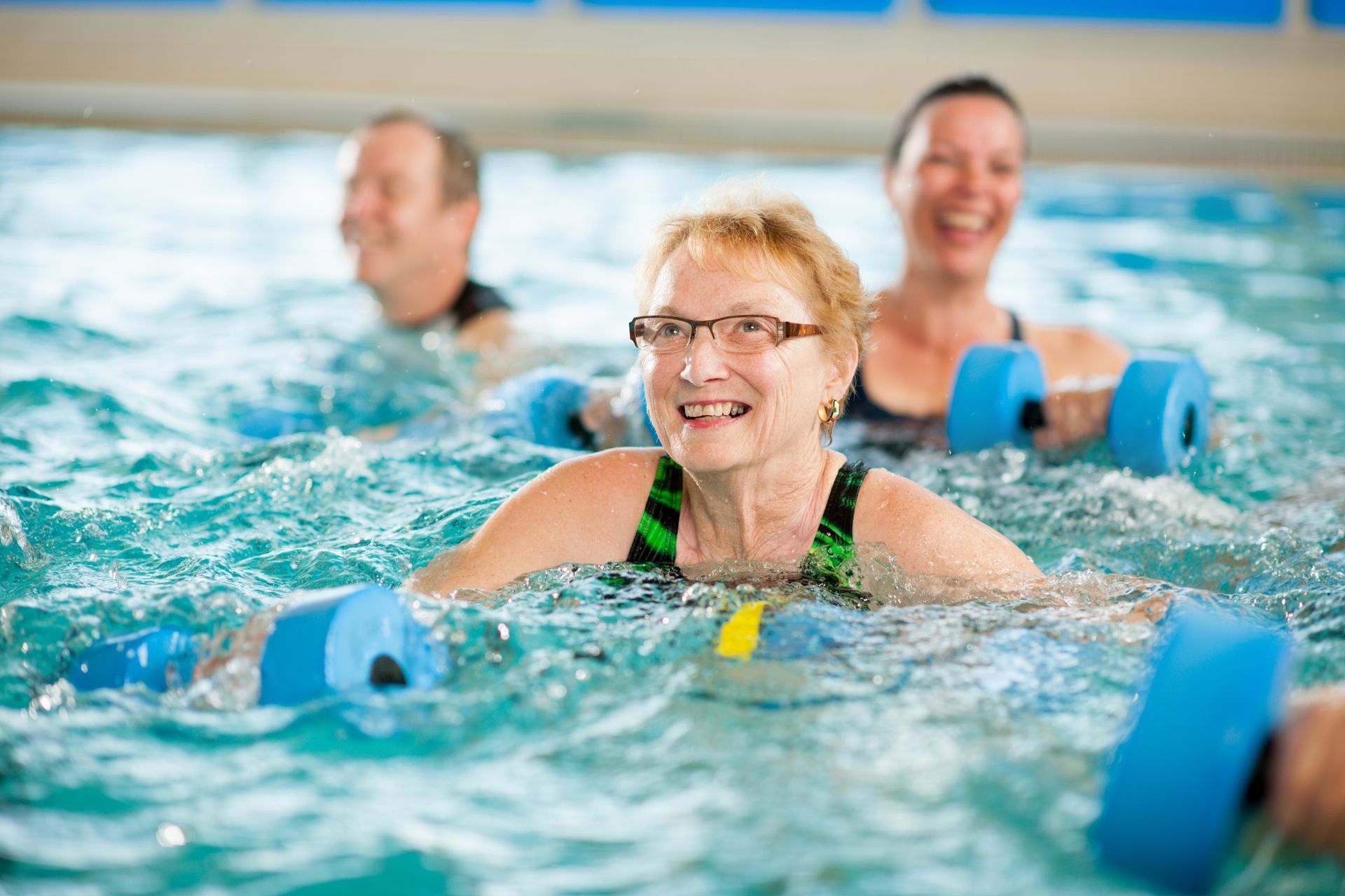 People exercising in a pool, holding blue foam dumbbells to perform water aerobics.