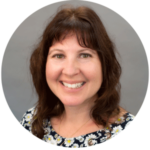 Woman with brown hair and a smiling expression, wearing a floral top against a gray backdrop.