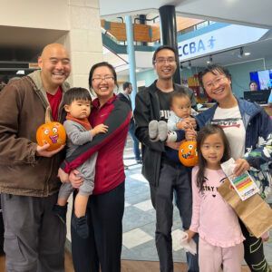 Two families with children holding painted pumpkins and smiles in a lobby.