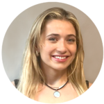 Blond woman with a big smile wearing a black necklace against a gray background.