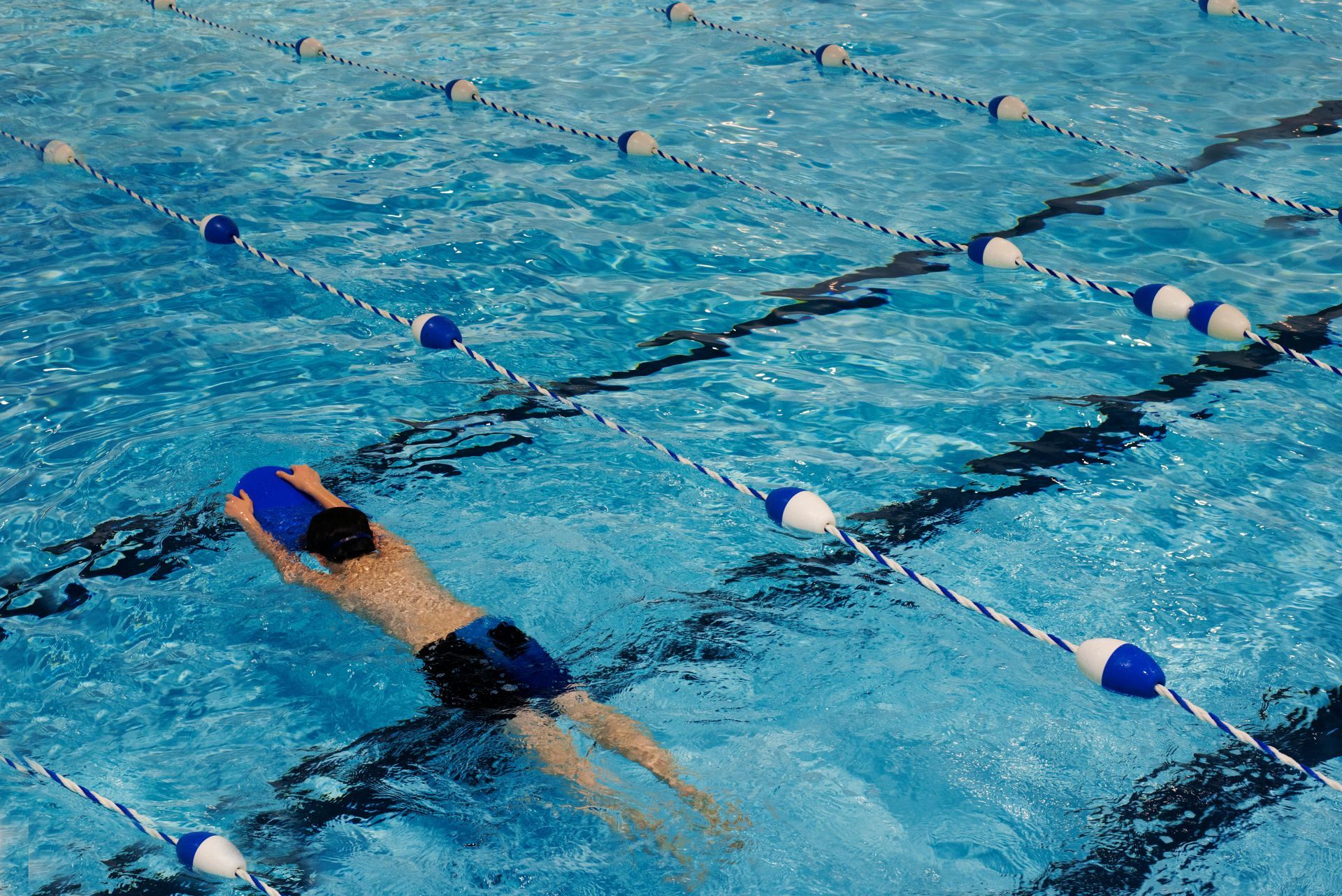Person swimming freestyle in a blue pool, lanes marked with floats.