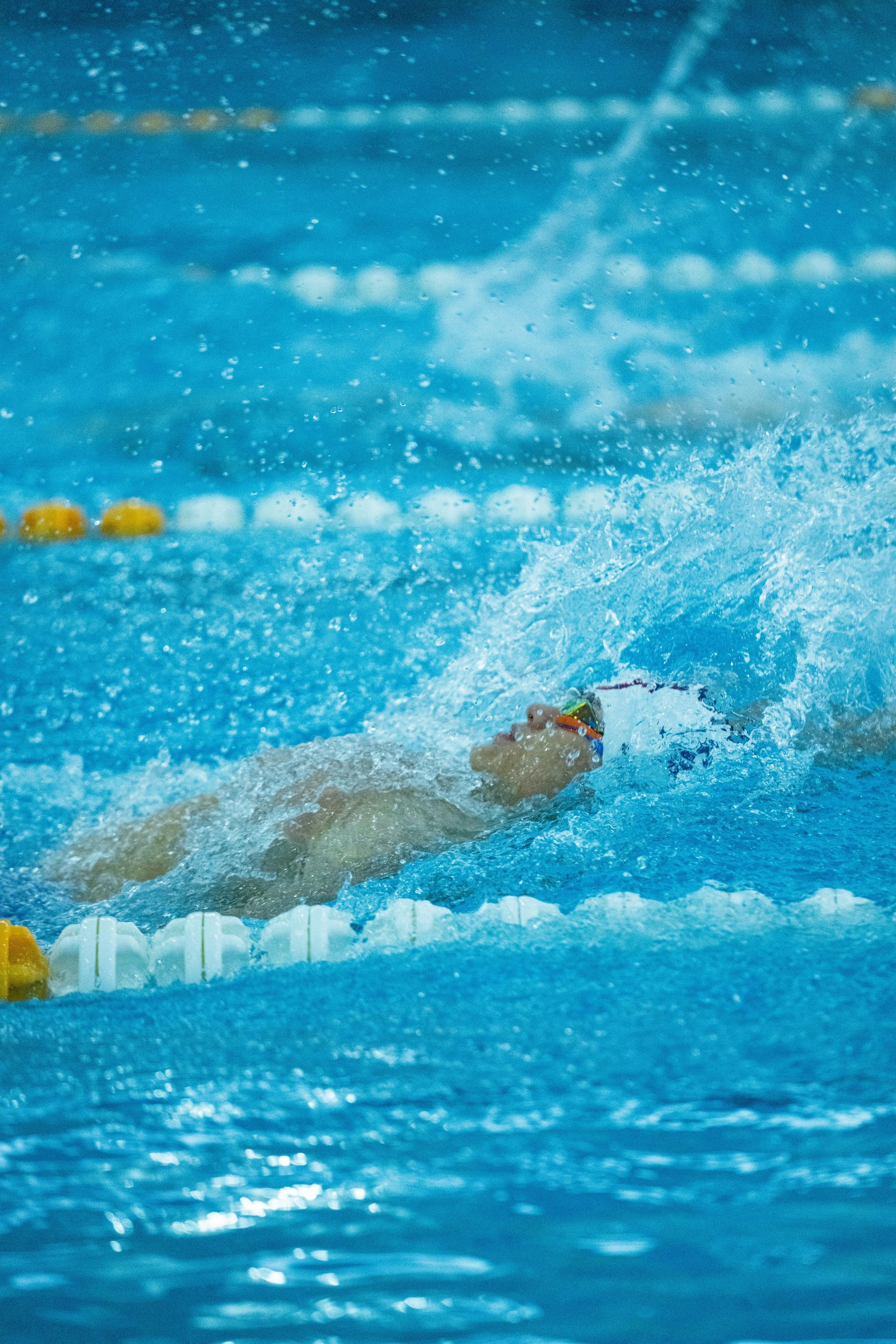 Swimmer in a blue pool, performing backstroke; water splashing.
