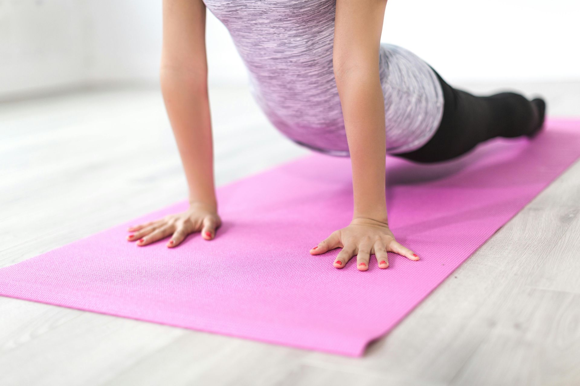 Woman doing a yoga pose on a pink mat in a bright room.