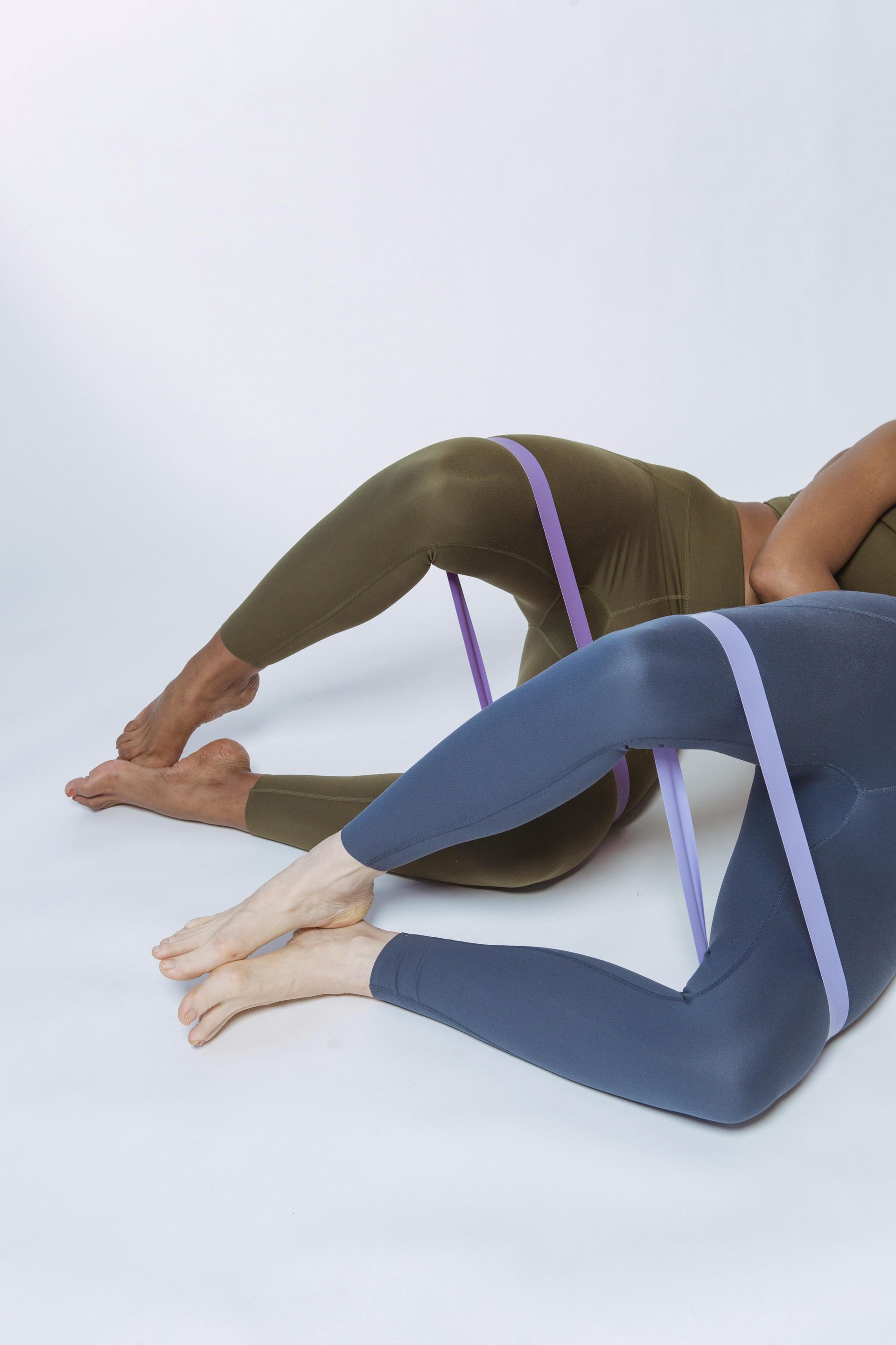 Two people exercising with resistance bands, lying on their sides, legs bent.