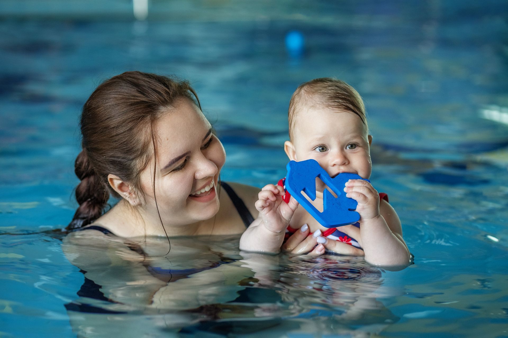 Group of swimmers smiling in a pool, posing near the edge. Some wearing swim caps and goggles.