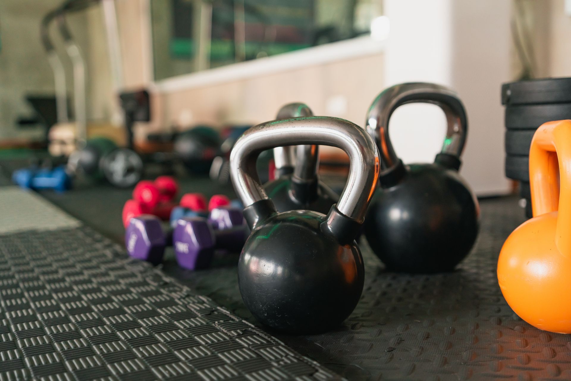 Various kettlebells and dumbbells arranged on a black rubber gym floor.