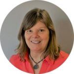 Woman in a coral shirt smiles, wearing a pendant, against a grey background.