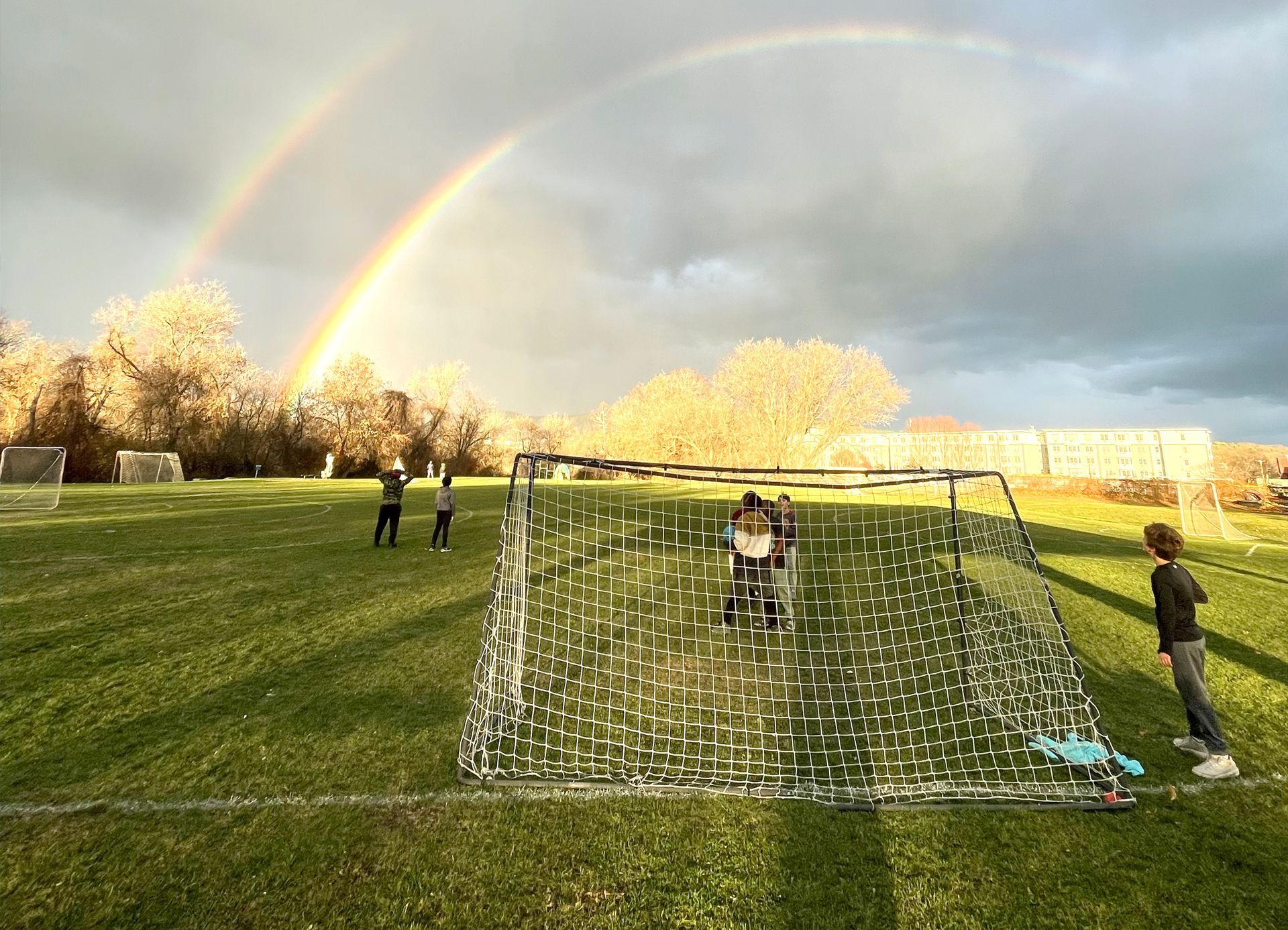 Children playing soccer on a grassy field with a double rainbow arching overhead.