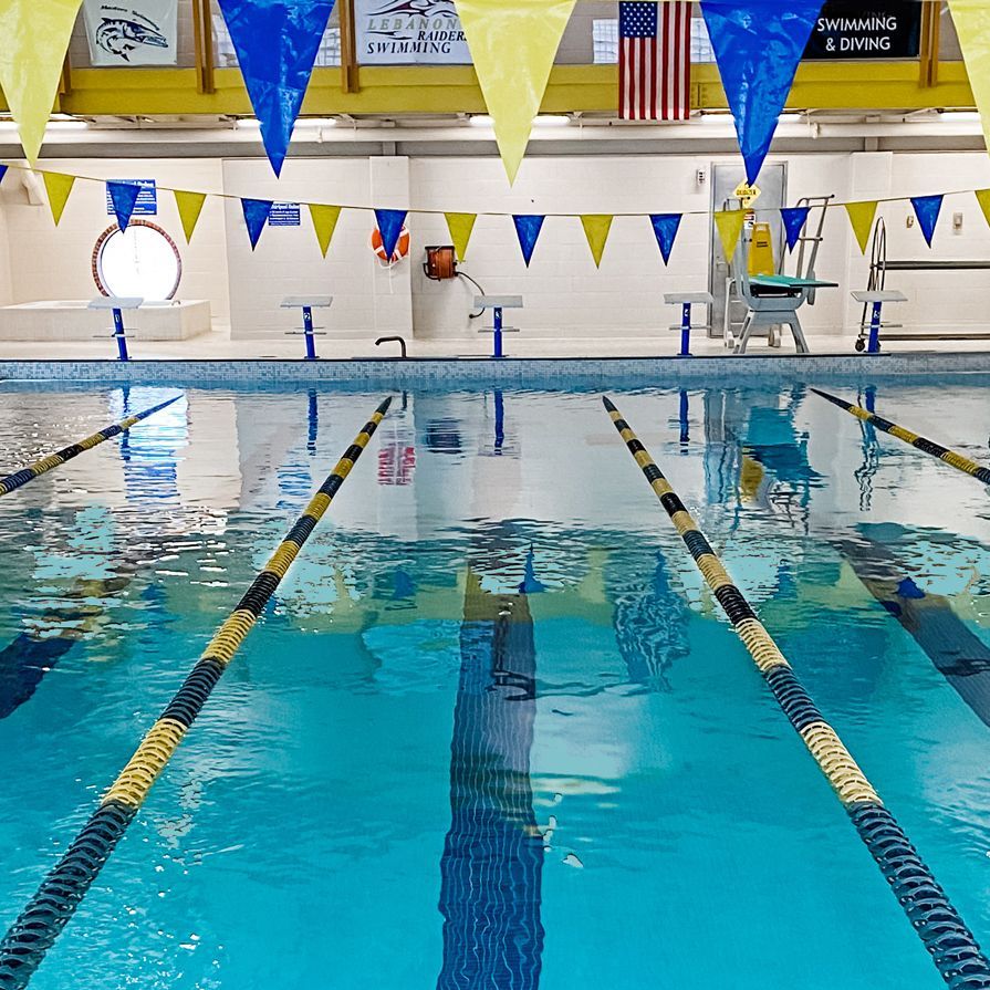 Indoor swimming pool with lanes marked by black and yellow lines. Blue and yellow pennant flags hang overhead.