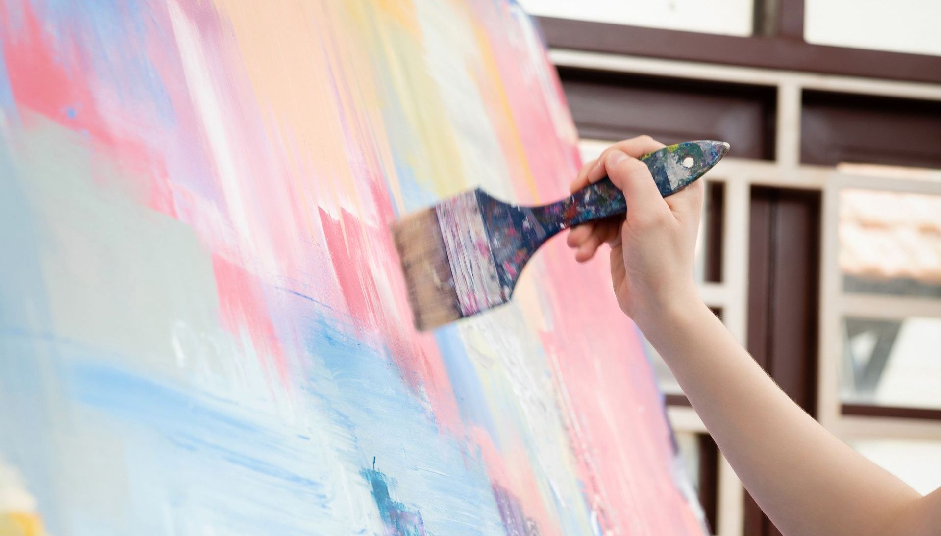 A person is holding a brush and painting on a canvas.