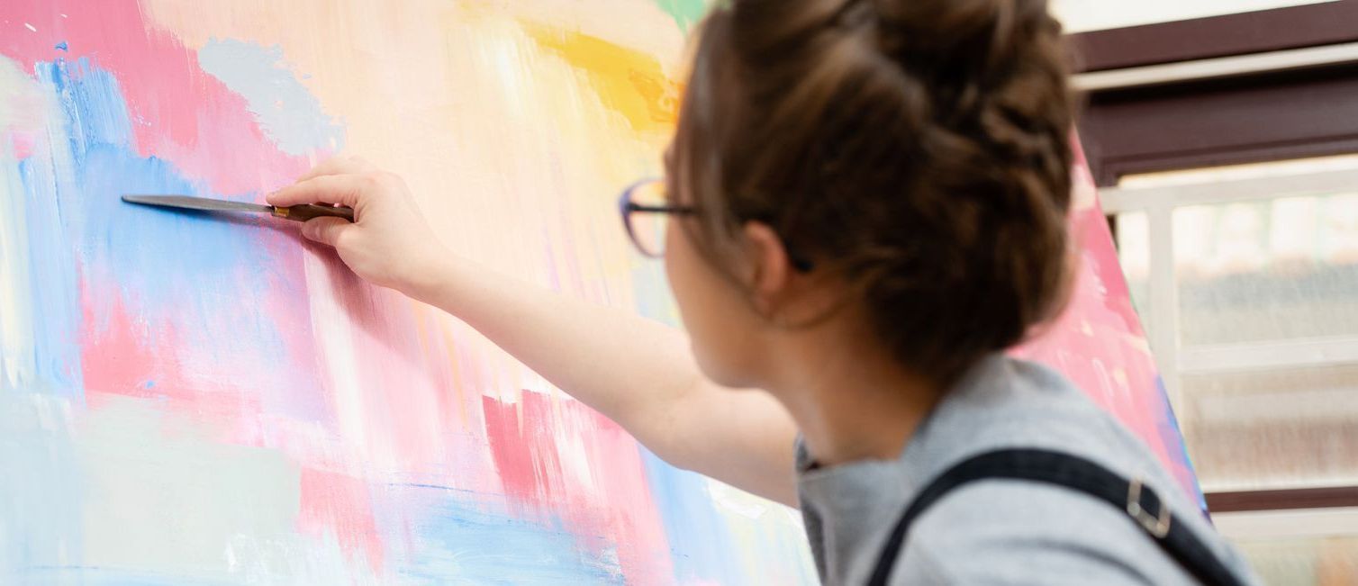 A woman is painting on a large canvas with a brush.