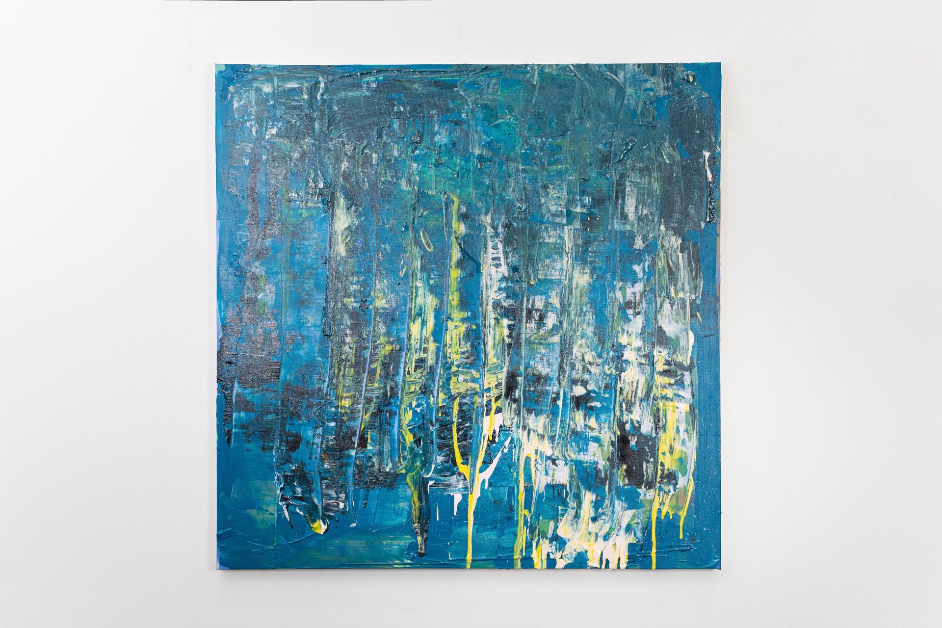 A blue and yellow abstract painting is hanging on a white wall.