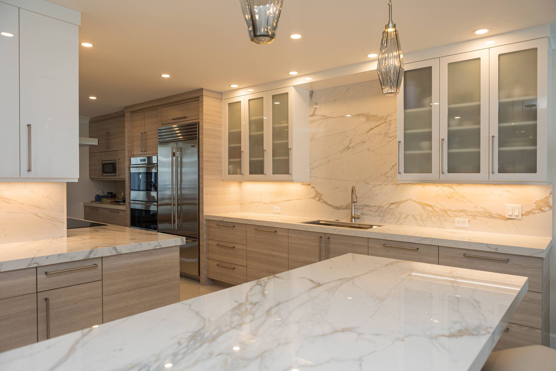 Modern kitchen with marble countertops, light wood cabinets, and stainless steel appliances.