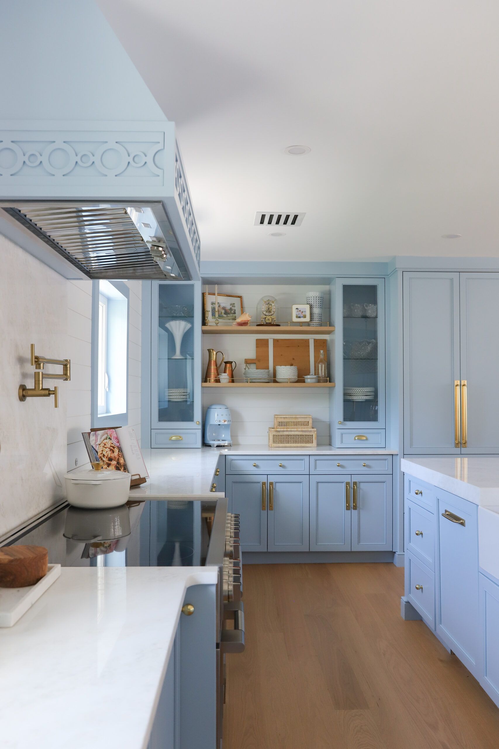 Blue kitchen with wooden floor, white countertops, stainless steel range hood, and gold hardware.